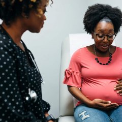 Black midwife talking with third trimester pregnant woman